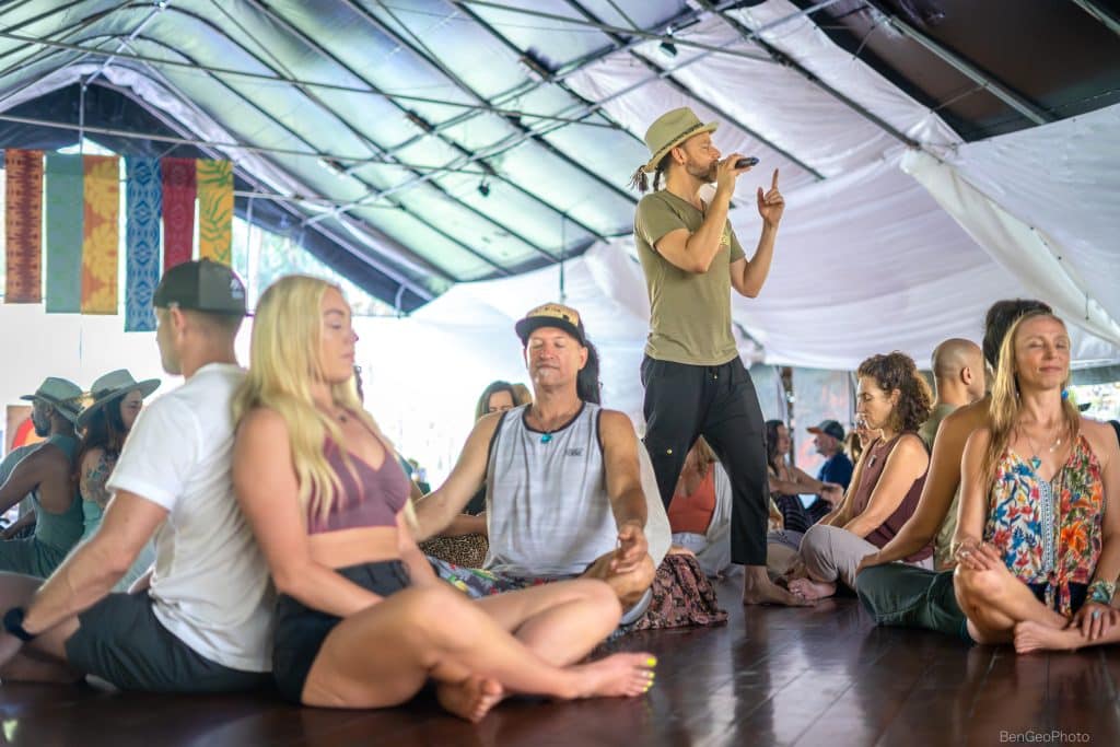 group at a movement event, sitting in groups of two with each person's back touching the other, meditating
