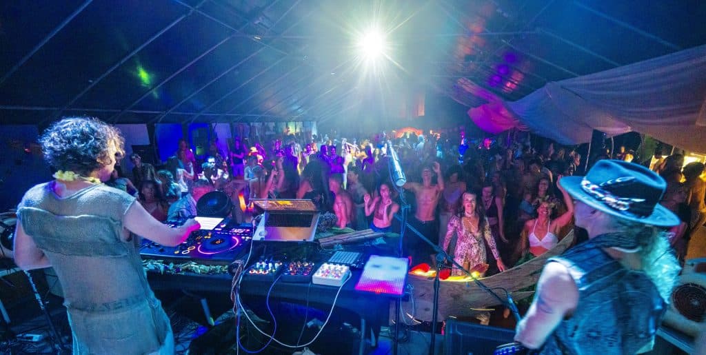 view from behind DJ on stage with crowd in front dancing at a movement event