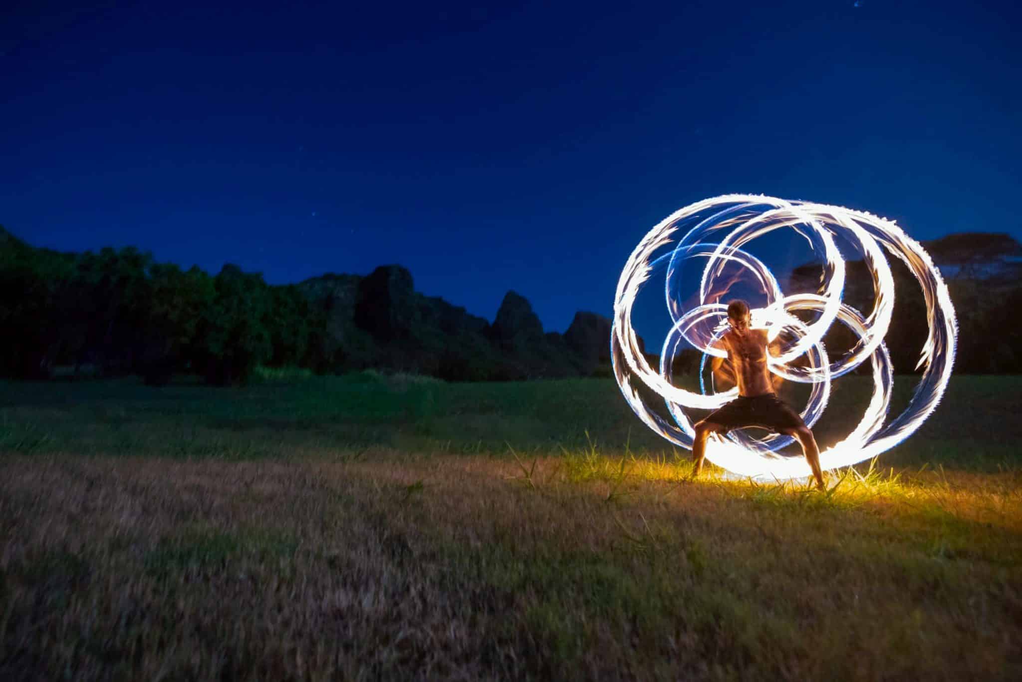 fire spinner outdoors in a field making a beautiful pattern in the air at a movement event ecstatic dance