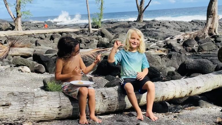 two kids sitting on log at beach together