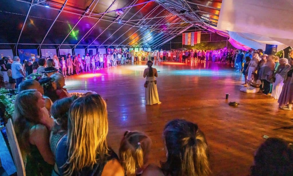 a native hawaiian woman dressed in ceremonial clothes standing in a circle of people holding hands at movement event